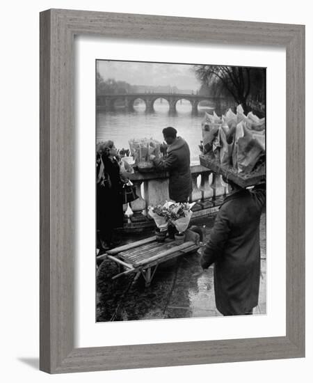 Parisian Flower Vendor at Work Stocking His Stall on the Seine with the Pont Neuf in the Background-Ed Clark-Framed Photographic Print