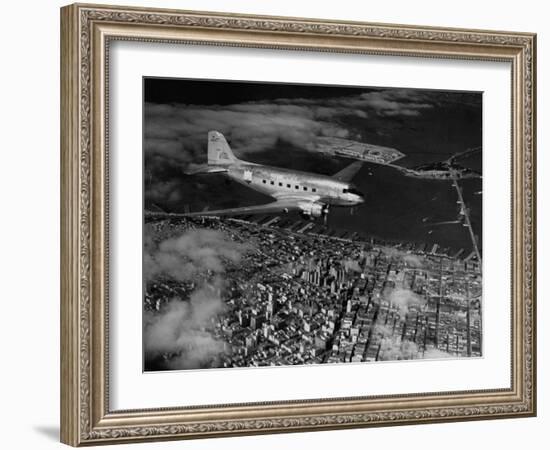 Plane Flying over a City from a Story Concerning United Airlines-Carl Mydans-Framed Photographic Print