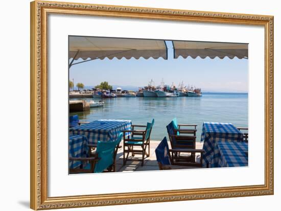 Platanias, Thessaly, Greece. Tables and chairs outside a harbour side restaurant. Fishing boats...-null-Framed Photographic Print