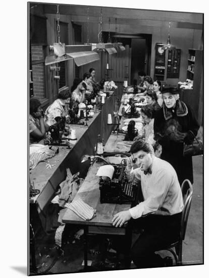 Playwright Paddy Chayefsky Sitting at Typewriter in Garment Factory With Workers on Sewing Machines-Michael Rougier-Mounted Premium Photographic Print