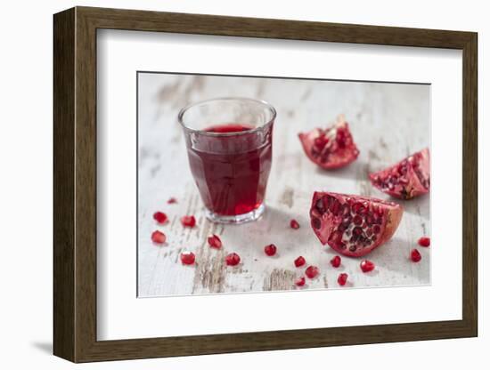 Pomegranate Pieces and a Glass of Pomegranate Juice on White Wooden Table-Jana Ihle-Framed Photographic Print