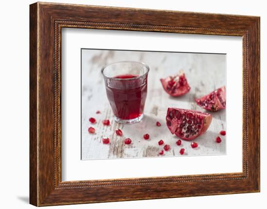 Pomegranate Pieces and a Glass of Pomegranate Juice on White Wooden Table-Jana Ihle-Framed Photographic Print