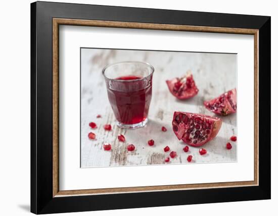Pomegranate Pieces and a Glass of Pomegranate Juice on White Wooden Table-Jana Ihle-Framed Photographic Print