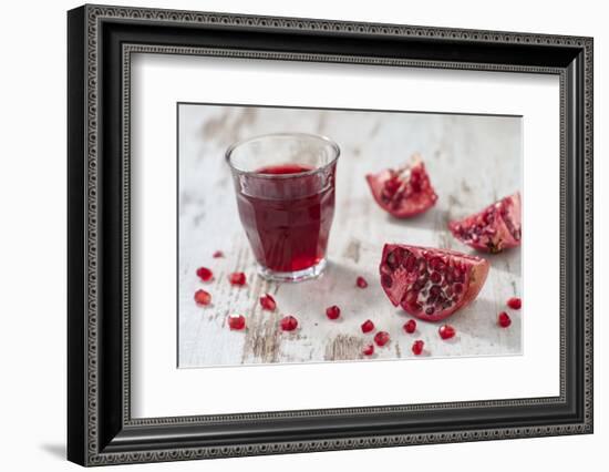 Pomegranate Pieces and a Glass of Pomegranate Juice on White Wooden Table-Jana Ihle-Framed Photographic Print