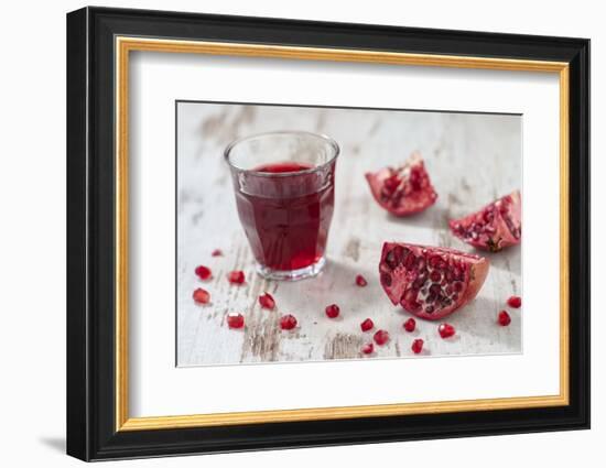 Pomegranate Pieces and a Glass of Pomegranate Juice on White Wooden Table-Jana Ihle-Framed Photographic Print