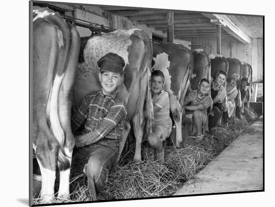 Row of Cows' Rumps, with Fat Cheeked Family of Six Milking Them, in Neat Cow Barn-Alfred Eisenstaedt-Mounted Photographic Print