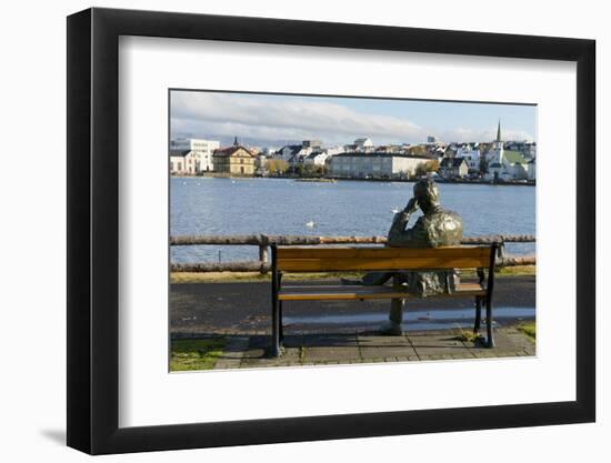 Sculpture of a man sitting on a park bench in front of Tjornin Lake and the Historic Centre of Rykj-Miles Ertman-Framed Photographic Print