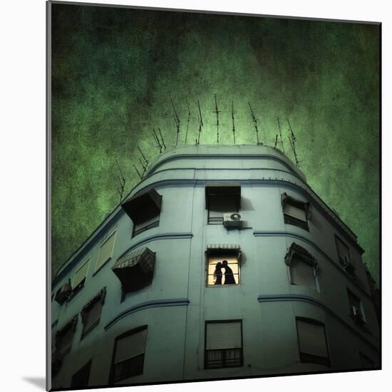Silhouette of a Man and Woman Kissing in a Window of a Large Building with TV Ariels on the Roof-Luis Beltran-Mounted Photographic Print