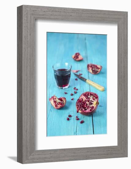 Sliced Pomegranate and a Glass of Pomegranate Juice on Turquoise Wooden Table-Jana Ihle-Framed Photographic Print