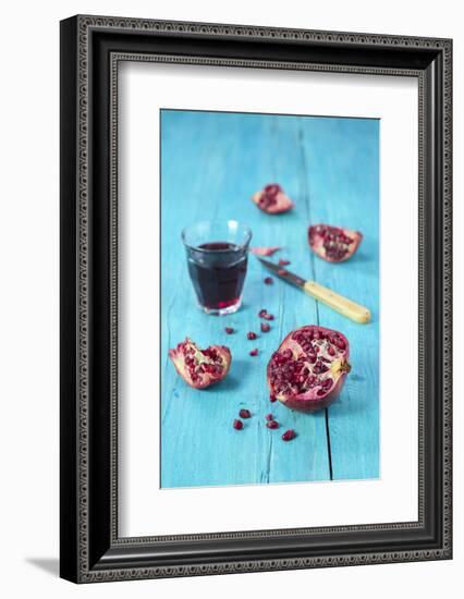 Sliced Pomegranate and a Glass of Pomegranate Juice on Turquoise Wooden Table-Jana Ihle-Framed Photographic Print