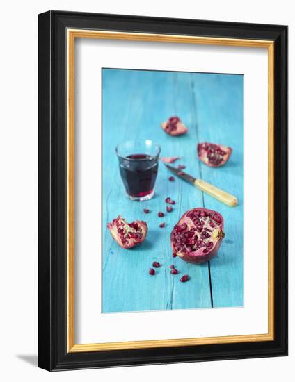 Sliced Pomegranate and a Glass of Pomegranate Juice on Turquoise Wooden Table-Jana Ihle-Framed Photographic Print