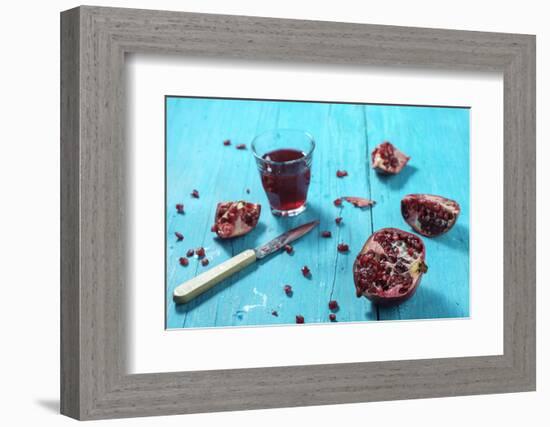 Sliced Pomegranate and a Glass of Pomegranate Juice on Turquoise Wooden Table-Jana Ihle-Framed Photographic Print