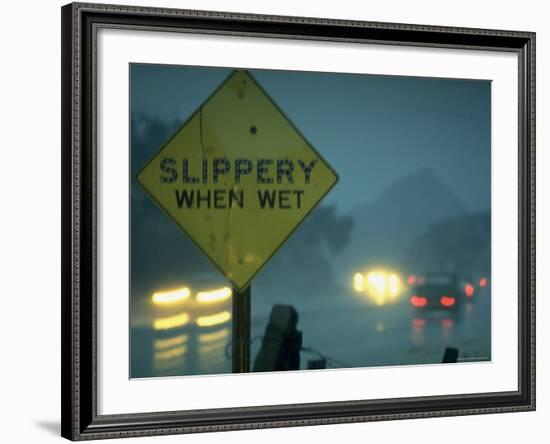 Slippery When Wet Sign in Fore with Traffic in Background in Rain on California Highway 14-Ralph Crane-Framed Photographic Print