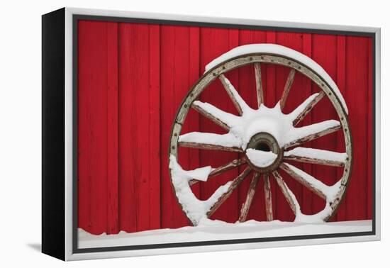 Snow-covered wagon wheels against red barn near town of Banff, Canadian Rockies, Alberta, Canada-Stuart Westmorland-Framed Premier Image Canvas