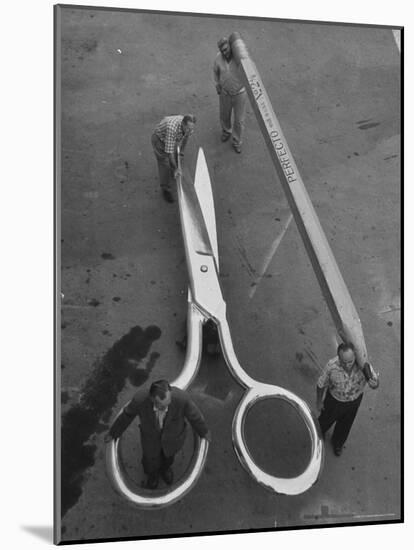 Stagehands Pushing a Pair of Gigantic Scissors on a Dollie Next to Two Men Carrying a 21 Ft. Pencil-Allan Grant-Mounted Photographic Print