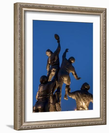 Statue of rugby players is illuminated at dusk outside Twickenham Stadium, London-Charles Bowman-Framed Photographic Print