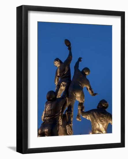 Statue of rugby players is illuminated at dusk outside Twickenham Stadium, London-Charles Bowman-Framed Photographic Print