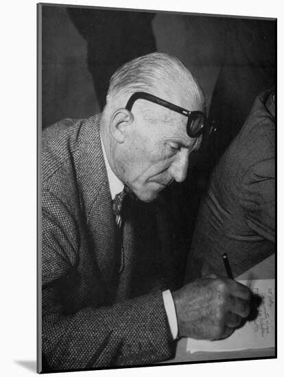 Swiss Architect Le Corbusier Leaning Down to Write with His Glasses Pushed Back on His Forehead-null-Mounted Photographic Print