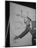 Swiss Architect Le Corbusier Standing on Stage with Notes in His Hand and Drawing on Sketch Pad-null-Mounted Photographic Print