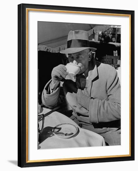 Syndicated Columnist Walter Winchell Clad in Overcoat and Gloves Drinking Coffee in Outdoor Patio-Alfred Eisenstaedt-Framed Premium Photographic Print