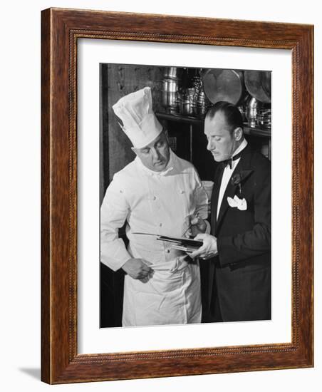 The 21 Club's Jack Kriendler Wearing a Tuxedo and Conferring with a Chef in the Club's Kitchen-null-Framed Photographic Print