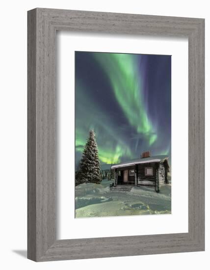 The Northern Lights (Aurora borealis) frame the wooden hut in the snowy woods, Pallas, Yllastunturi-Roberto Moiola-Framed Photographic Print