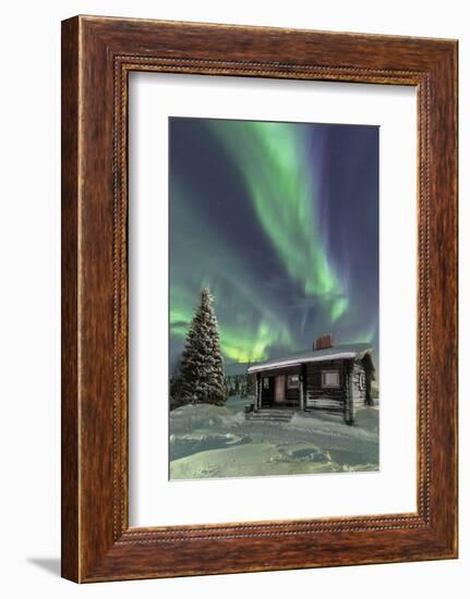 The Northern Lights (Aurora borealis) frame the wooden hut in the snowy woods, Pallas, Yllastunturi-Roberto Moiola-Framed Photographic Print