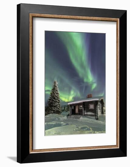 The Northern Lights (Aurora borealis) frame the wooden hut in the snowy woods, Pallas, Yllastunturi-Roberto Moiola-Framed Photographic Print