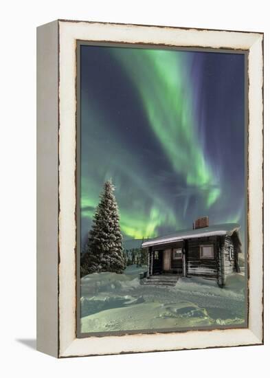 The Northern Lights (Aurora borealis) frame the wooden hut in the snowy woods, Pallas, Yllastunturi-Roberto Moiola-Framed Premier Image Canvas