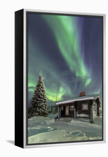 The Northern Lights (Aurora borealis) frame the wooden hut in the snowy woods, Pallas, Yllastunturi-Roberto Moiola-Framed Premier Image Canvas