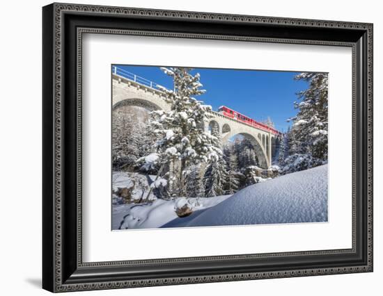 The red train on viaduct surrounded by snowy woods, Cinuos-Chel, Canton of Graubunden, Engadine, Sw-Roberto Moiola-Framed Photographic Print