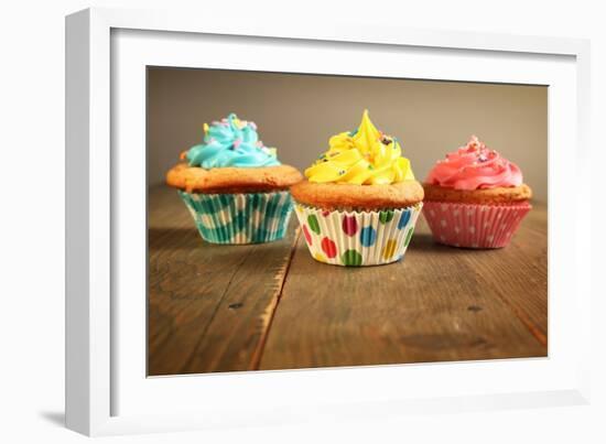 Three Different Colors Cupcakes On A Wooden Table, Blue, Yellow And Pink-pink candy-Framed Art Print