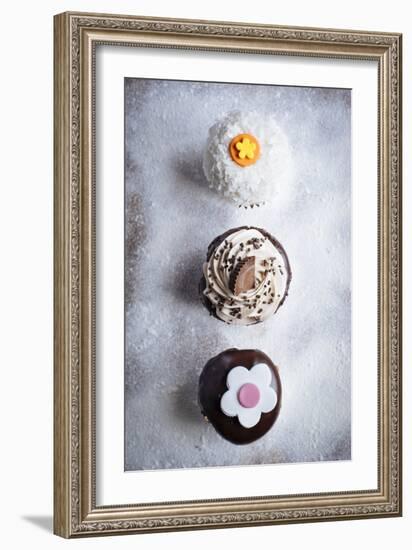 Three Different Cupcakes, Coconut, Peanut Butter And Chocolate Arranged In A Line On A Sifted Flour-Shea Evans-Framed Photographic Print