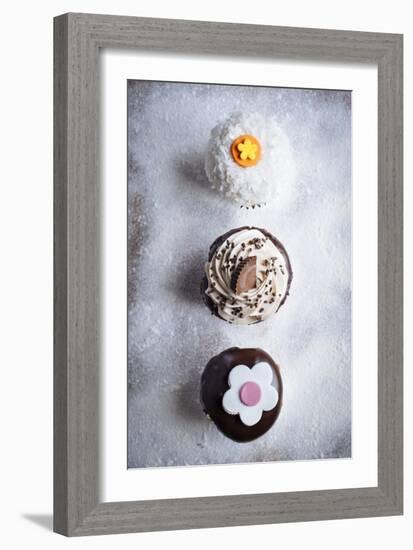 Three Different Cupcakes, Coconut, Peanut Butter And Chocolate Arranged In A Line On A Sifted Flour-Shea Evans-Framed Photographic Print