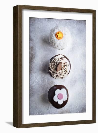 Three Different Cupcakes, Coconut, Peanut Butter And Chocolate Arranged In A Line On A Sifted Flour-Shea Evans-Framed Photographic Print