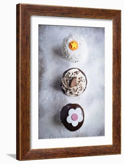 Three Different Cupcakes, Coconut, Peanut Butter And Chocolate Arranged In A Line On A Sifted Flour-Shea Evans-Framed Photographic Print