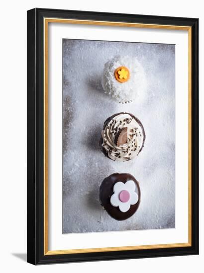 Three Different Cupcakes, Coconut, Peanut Butter And Chocolate Arranged In A Line On A Sifted Flour-Shea Evans-Framed Photographic Print