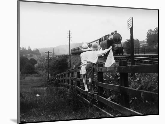 Two Children Stand on a Fence and Wave a Handkerchief at a Passing Steam Train-Staniland Pugh-Mounted Photographic Print