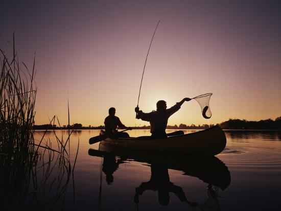 Two Men Catching Fish In Canoe At Sunset Photographic Print By
