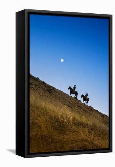 Two wranglers riding horses up a hill with full moon in background at blue hour-Sheila Haddad-Framed Premier Image Canvas