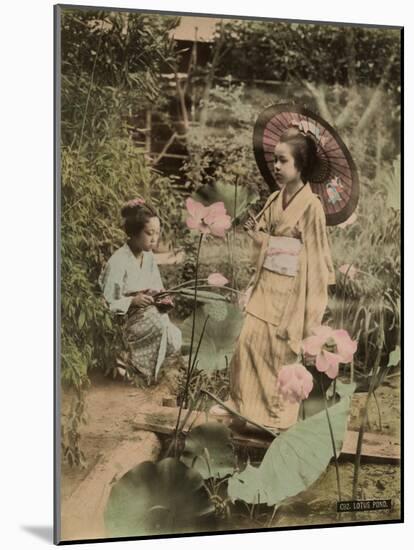 Two Young Japanese Girls, One Holding a Parasol, with Lotus Flowers-null-Mounted Photographic Print