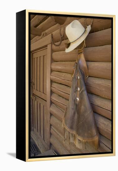 USA, Montana, Livingston, cowboy hat and chaps hanging on barn wall.-Merrill Images-Framed Premier Image Canvas