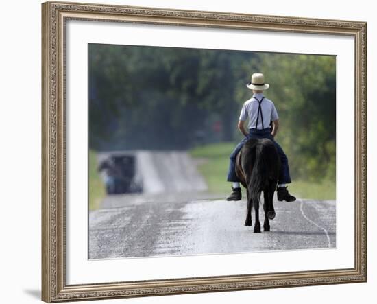 With a Buggy Approaching in the Distance, an Amish Boy Heads Down a Country Road on His Pony-Amy Sancetta-Framed Photographic Print