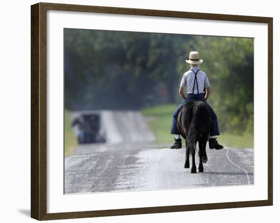 With a Buggy Approaching in the Distance, an Amish Boy Heads Down a Country Road on His Pony-Amy Sancetta-Framed Photographic Print