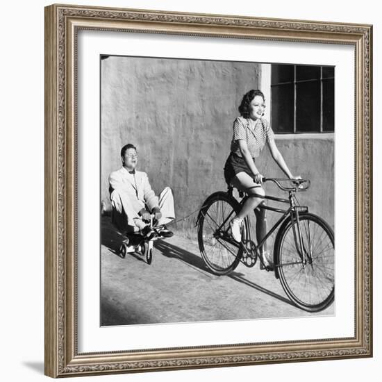 Woman on a Bicycle Pulling a Grown Man on a Toy Tricycle-null-Framed Photo