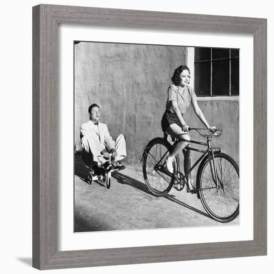 Woman on a Bicycle Pulling a Grown Man on a Toy Tricycle-null-Framed Photo