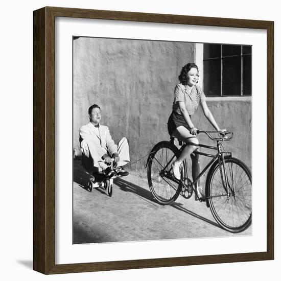 Woman on a Bicycle Pulling a Grown Man on a Toy Tricycle-null-Framed Photo