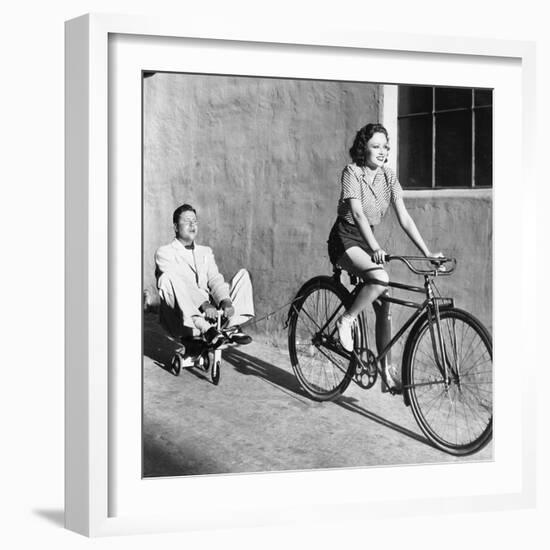 Woman on a Bicycle Pulling a Grown Man on a Toy Tricycle-null-Framed Photo