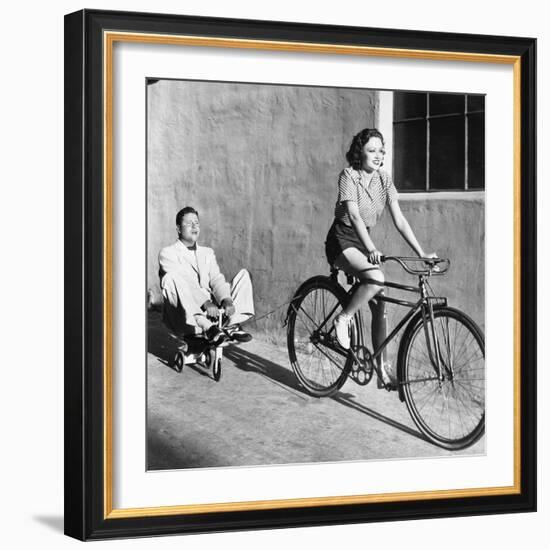 Woman on a Bicycle Pulling a Grown Man on a Toy Tricycle-null-Framed Photo