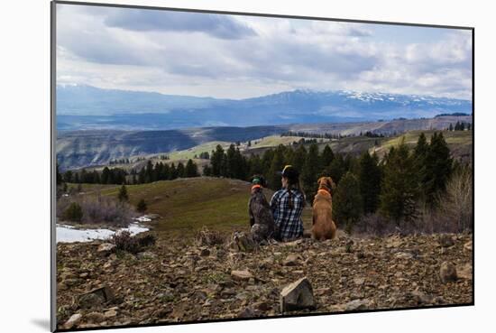 Woman Sits Next To Her Two Dogs Looking Out Into Idaho's Mountainous Landscape-Hannah Dewey-Mounted Photographic Print